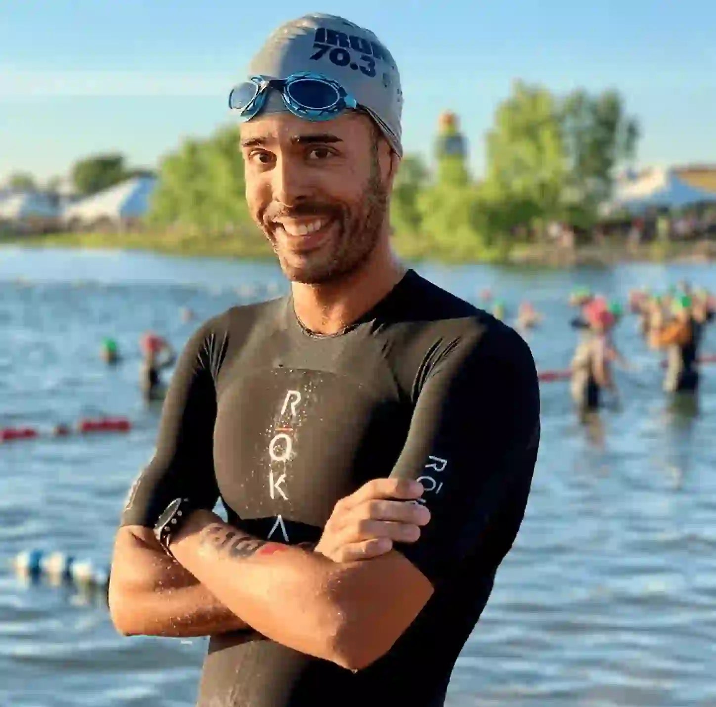 Breno Melo at the swim start of Boulder Ironman 70.3, wearing a wetsuit and smiling by the water, with other athletes in the background