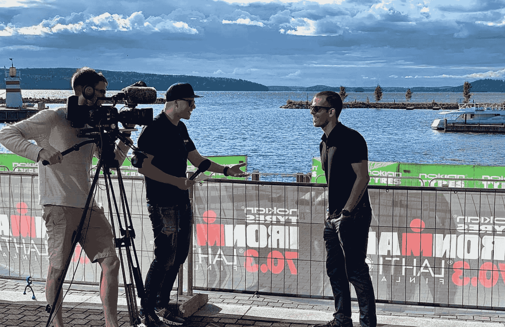 Breno Melo being interviewed by a film crew about Ironman coaching at a waterfront venue