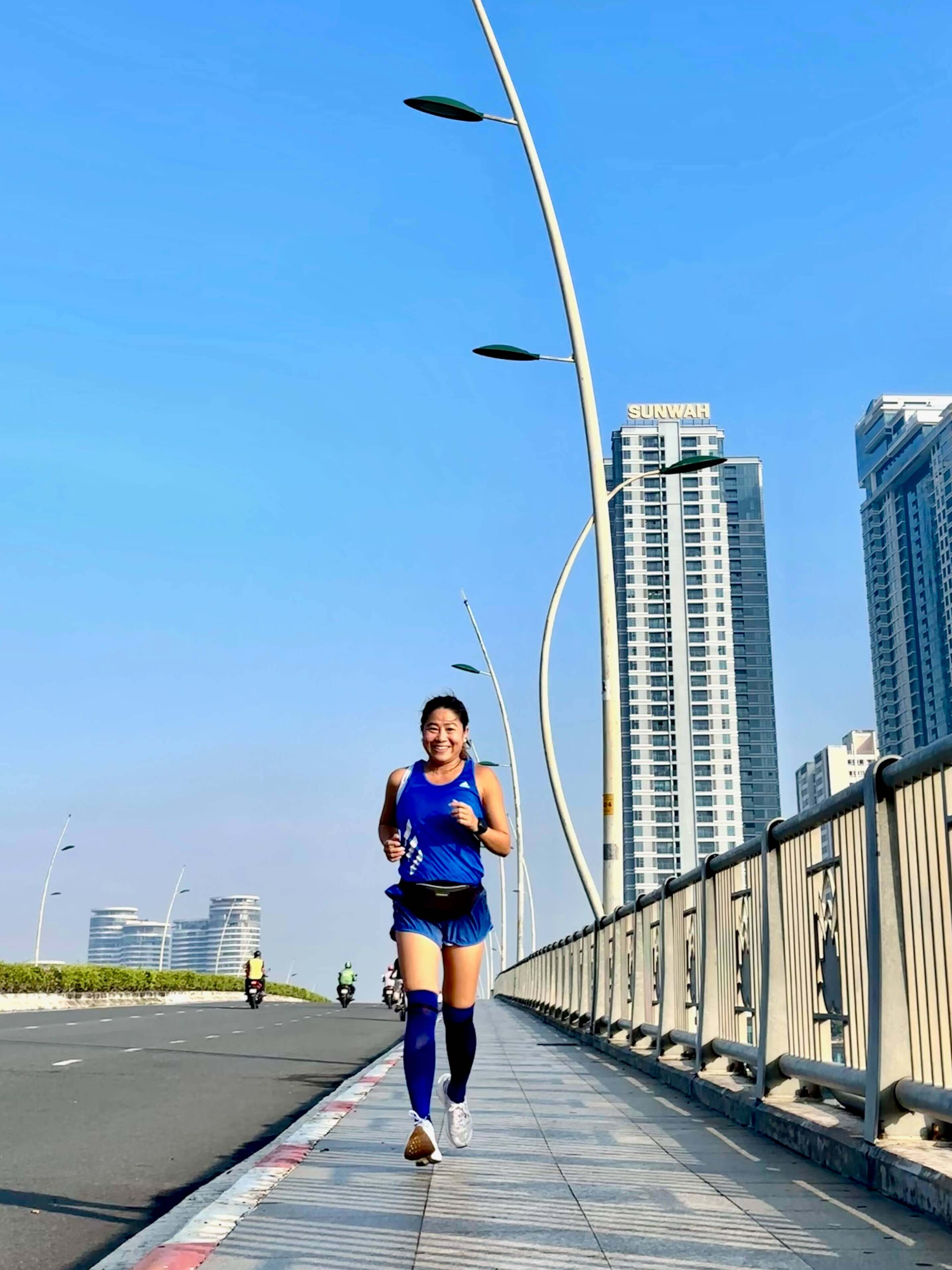 Boston Marathon finisher and business owner running on a bridge with city buildings in the background.