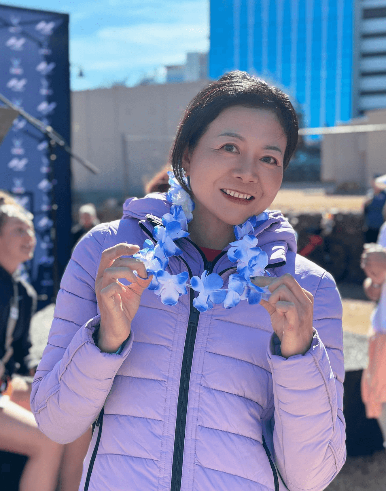 Heidi Die Wu smiling and wearing a blue floral lei at an event.