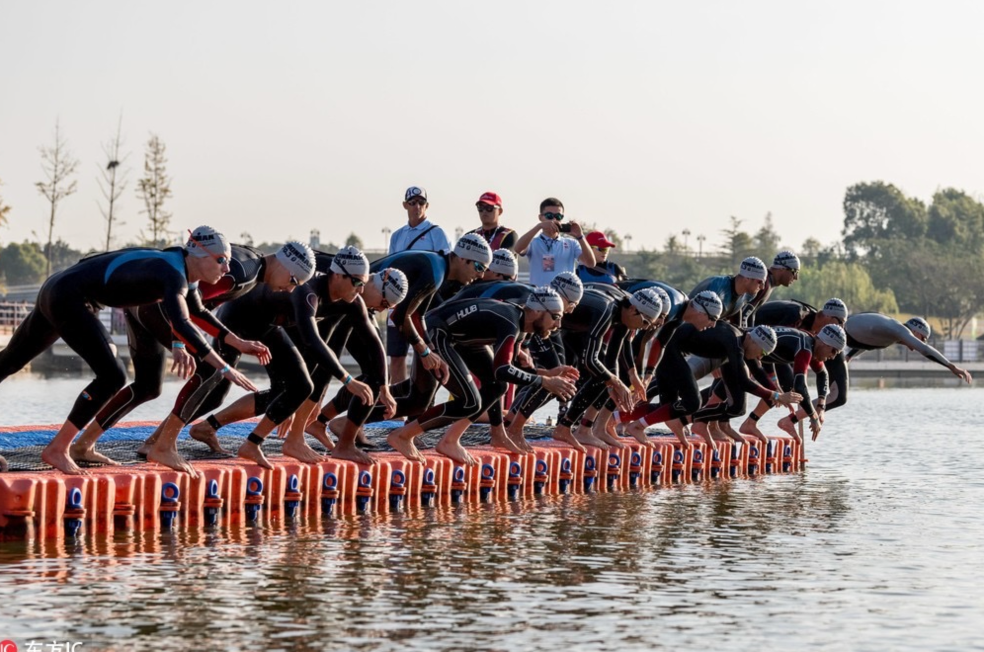 Triathletes in wetsuits preparing to dive into the open water at the swim start of a triathlon